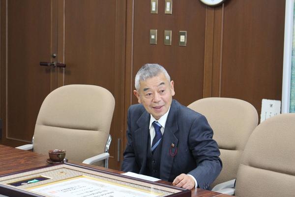 テーブルには、額に入った賞状が置いてあり、田渕清彦さんが座っている写真