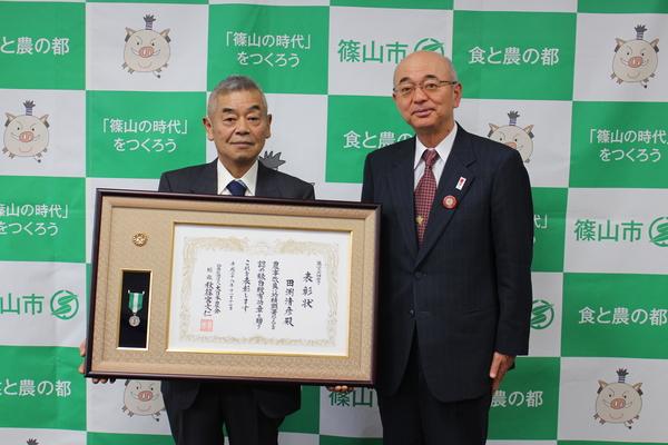 田渕清彦さんが額に入った賞状を持ち、市長と記念写真