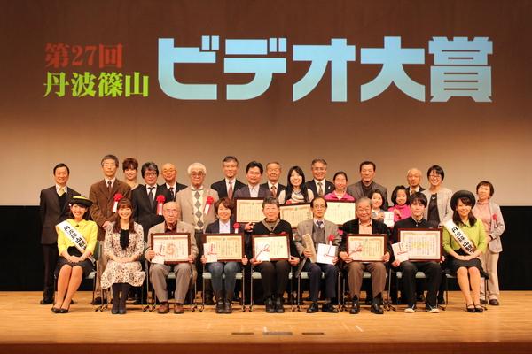 第27回丹波篠山ビデオ大賞と後のスクリーンに映しだされており、受賞をした参加者の前が額縁に入った賞状を持って笑顔で写っている集合写真