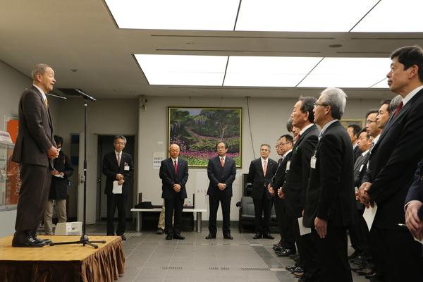 壇上のマイクに向かって林議長が話しをしているのを整列した職員が聞いている前方の写真