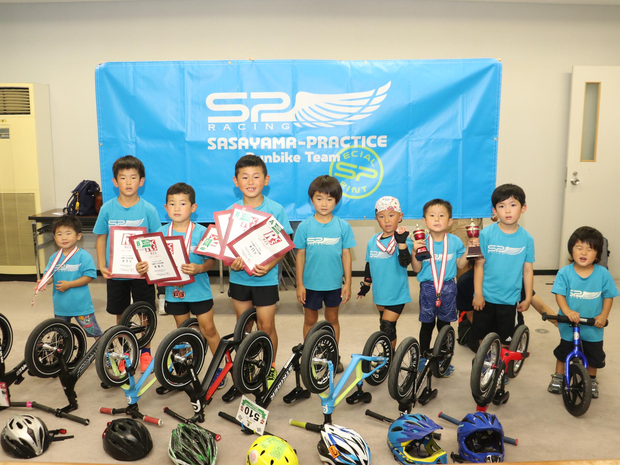 自転車とヘルメットを床に置いて、その後ろに子どもたちが並んでいる