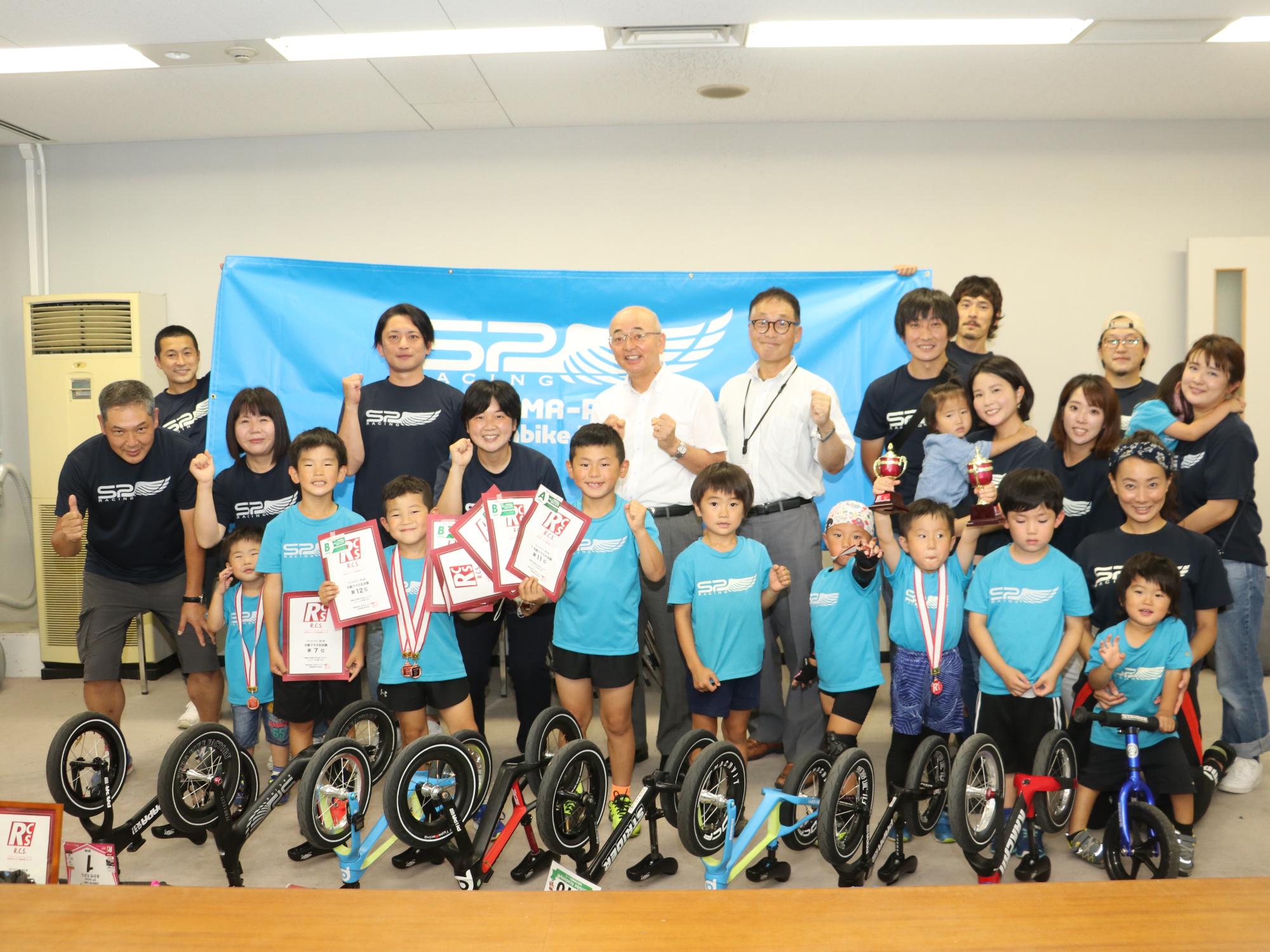 自転車を床に置いて、その後ろに子どもたちや保護者、市長、教育長が並んでいる