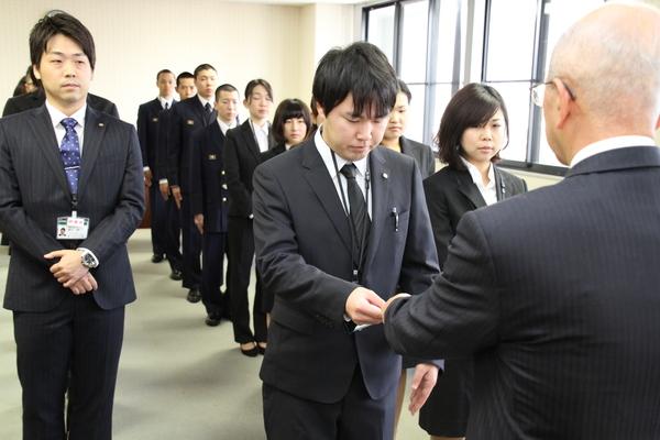 スーツを着た新規職員20名が整列し、代表の男性1名が市長の前に立っている写真