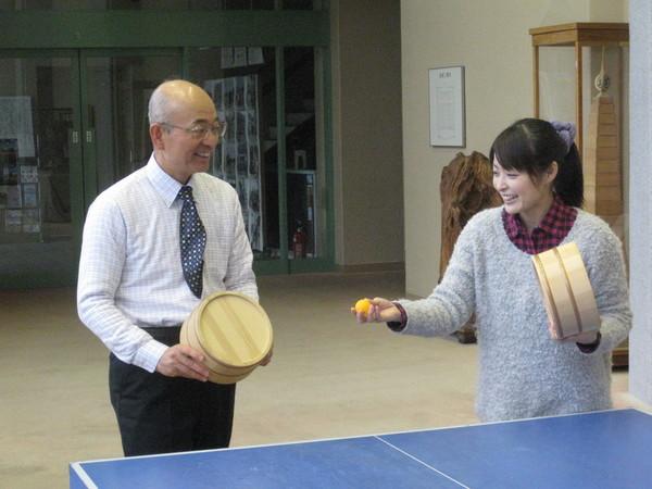 卓球台の前で熊谷 奈美さんが左手に桶を右手で卓球ボールを持ち、桶を持った市長に投げようとしている写真