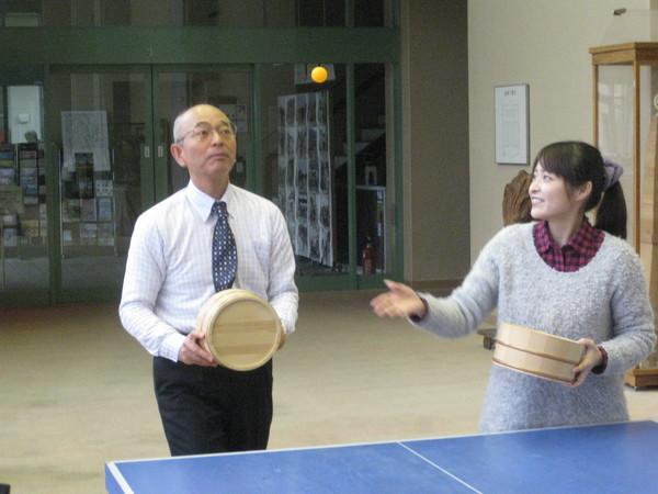 卓球台の前で熊谷 奈美さんが投げた卓球ボールを市長が桶で受けようとしている写真