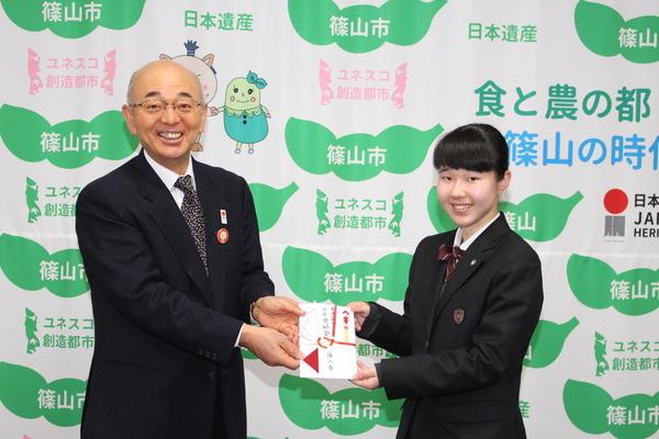 笑顔の女子生徒が、市長から金一封を受け取っている写真