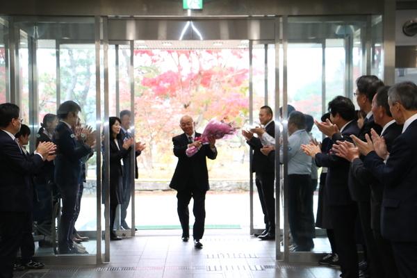 玄関で職員に囲まれ、市長が花束を持って入って来ている写真