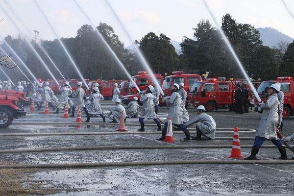 消防団員らが消防車のホースを持ち、放水演習を行っているのを左側から撮影されている写真