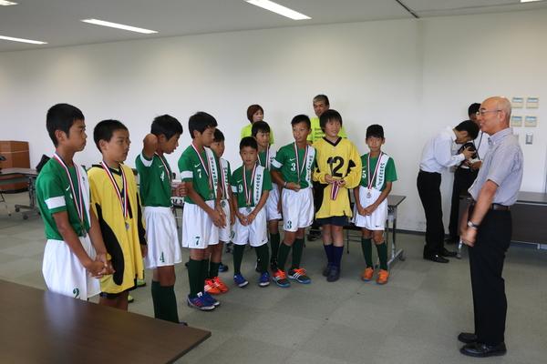 メダルをかけた10名のジュニアホッケーの部員たちが市長の前に横並びに並んでいる写真