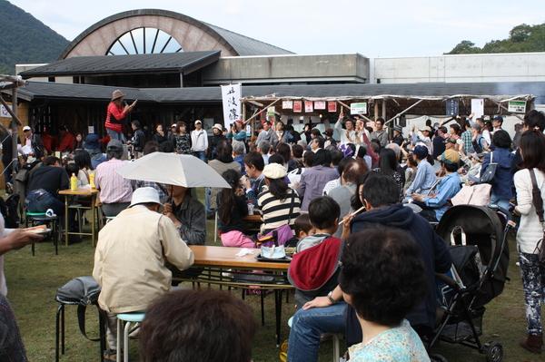 沢山の人が集まるなか、舞台の上でマイクを持っている女性の写真