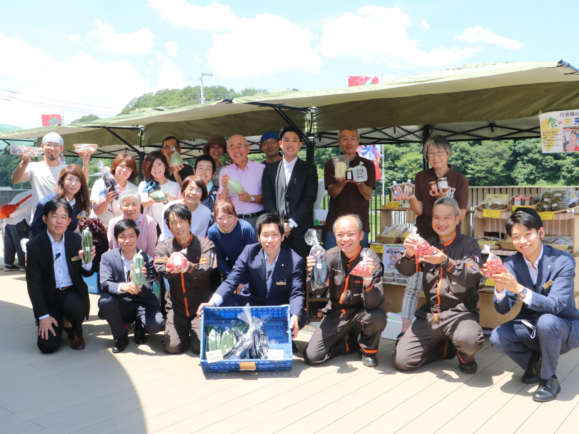 市場を訪れた方や主催者が野菜を手に持って記念撮影