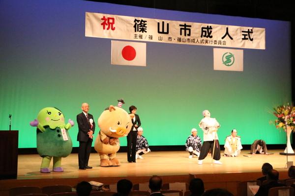 篠山市成人式で、舞台上にいるゆるキャラのまるいの、まめりん、市長の横で、衣装を着た黄門さまが高笑いをしている写真