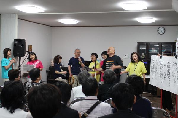 8名の男女がピアノやタンバリンなどに合わせて歌っている写真