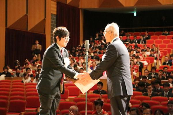 舞台上で、新成人の男女を前に、男性が、市長と握手をしている写真