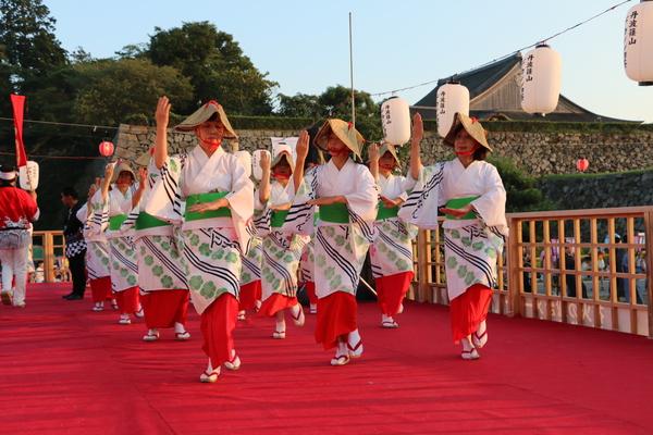 舞台の上で、浴衣に編み笠をかぶり踊る女性たちの写真