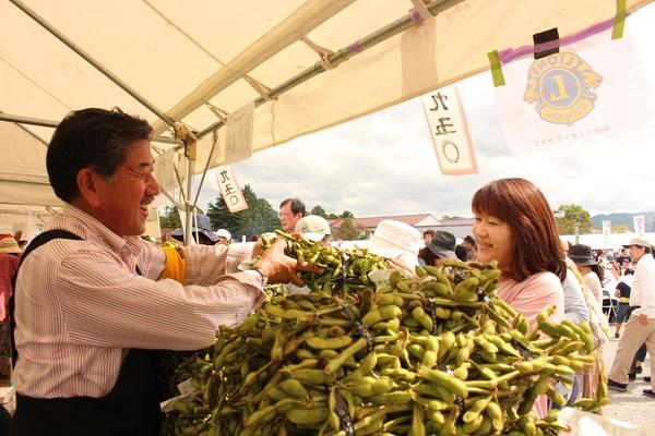 テントの中で山盛りに積まれた枝豆をお客さんに笑顔で販売している写真