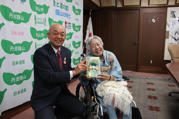車いすに乗った、藤木千皓さんと市長で募金を持って記念写真