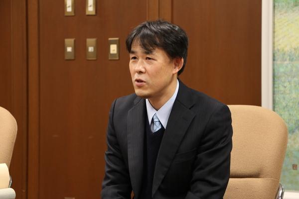 椅子に座っている高見先生の上半身の写真