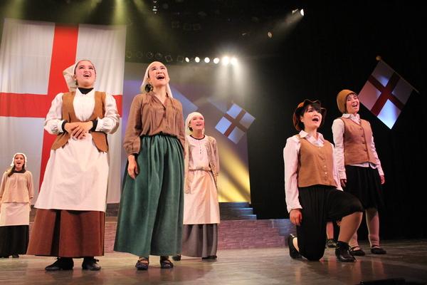 頭に三角巾を被り衣装を着た女性や右足を床につけた女性が遠くを見ながら歌っている様子の写真