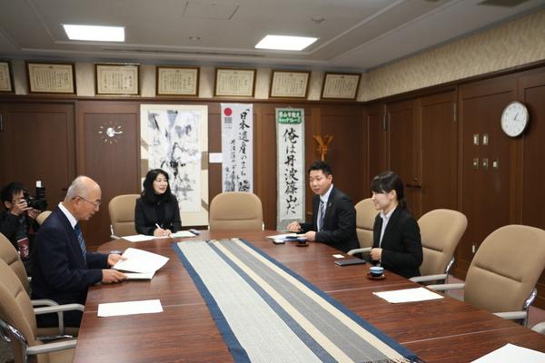 市長室にて、中西 美加さんが市長と向かい合って座っており、報告をしている様子の写真