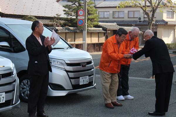 市長から鍵を渡される西紀中オレンジジャンパーの方が頭を下げ受け取っている写真