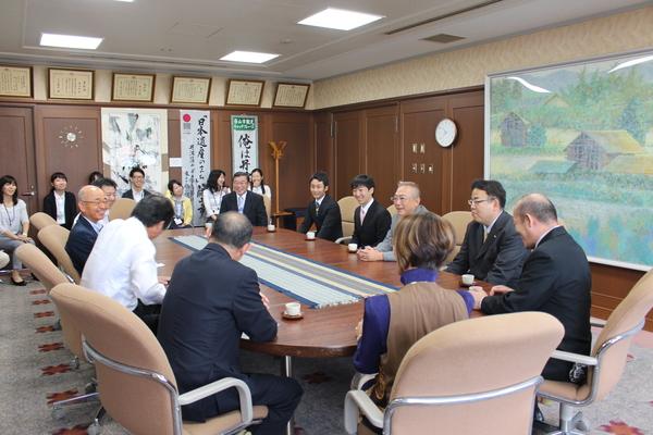 市長と渋谷さんが向かい合わせに座っていて、その周りに10人くらいの関係者が座っている写真