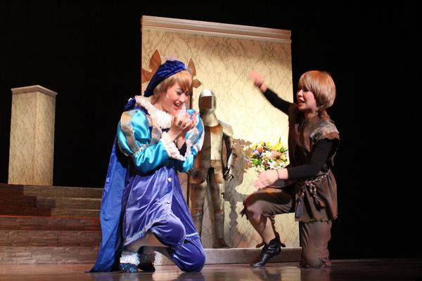 紫と水色の衣装を着てベレー帽を被っている主人公役の女性と茶色の衣装を着た主人公役の女性が片足を床につけ、動きを表している写真