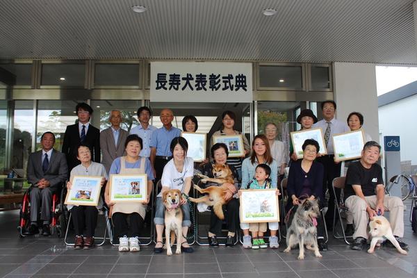 表彰された飼い主の方々が表彰状を持ち、犬や市長らと一緒に記念撮影している写真