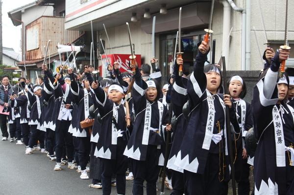 刀を上に振りかざしながら練り歩く子ども義士行列の写真