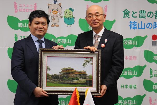 市長とスーツ姿の男性が額縁に入った絵画を二人で持っている写真