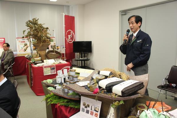 特産物をテーブルに並べ、男性が立って紹介している写真