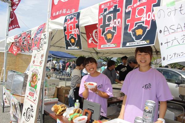 テントの中で女性販売の方が笑顔で丼ぶりを持ってる写真