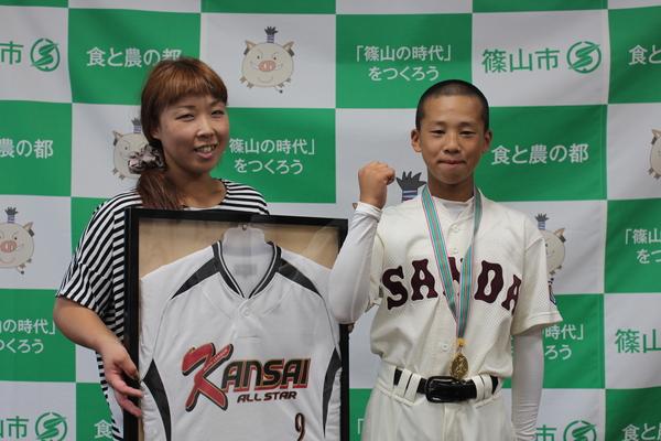 萱野 咲也さんのお母さんがユニフォームの入ってる額を持ち、咲也さんはメダルを首にかけてガッツポーズしている写真