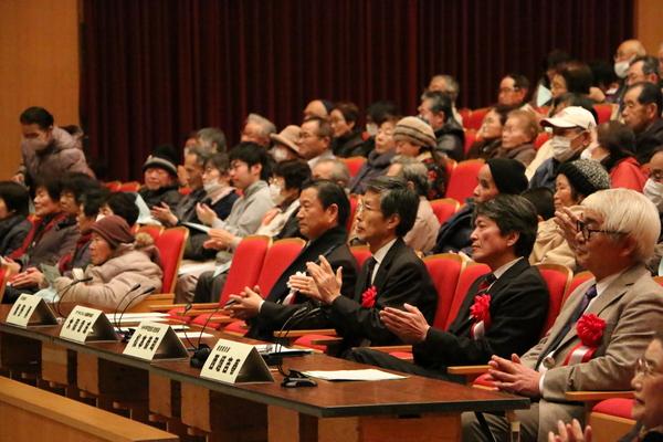 客席の一番前に作られている審査員席に胸に赤い胸章を付けた審査員が座っており、後にも沢山のお客さんが座っている様子の写真