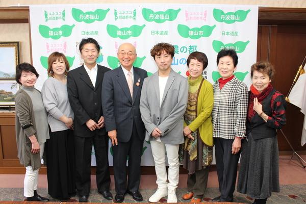 篠山市のタペストリーをバックに篠山市高齢者・障がい者訪問理美容サービス事業のサービス提供店7名と市長との記念写真