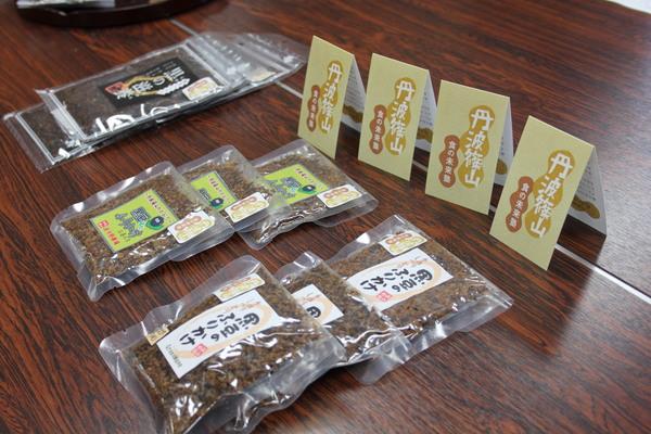 透明のパッケージの中央に黒色と緑色、白色のラベルが貼られてある新発売された黒豆ふりかけ3種類を長机の上に3袋ずつ縦に並んで置いてある写真