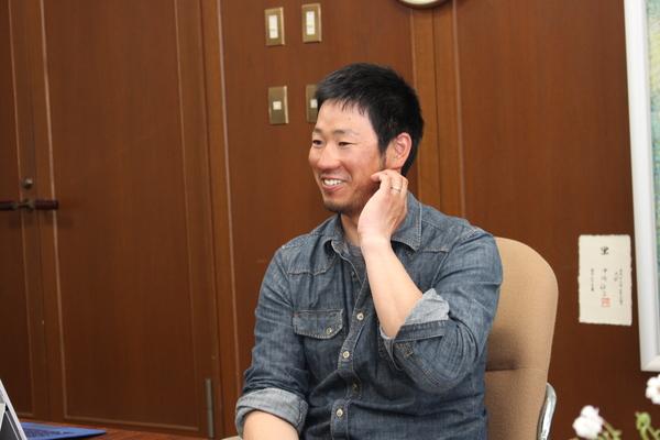 平井 駿也（ひらい しゅんや）さんが椅子に座り、笑顔で横顔の写真