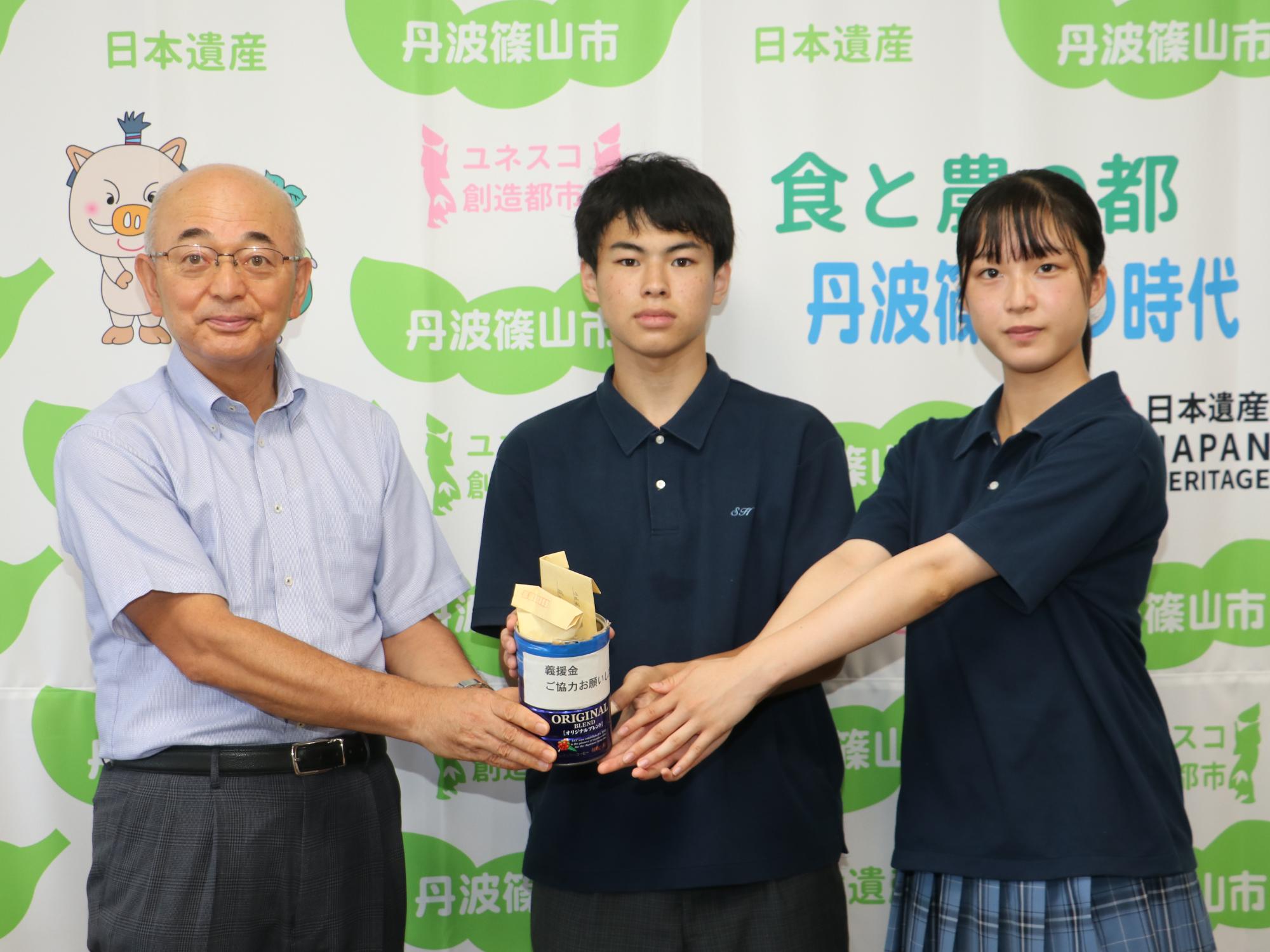 制服を着た男子高校生と女性高校生が集めた募金と一緒に市長と記念撮影
