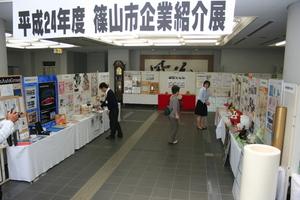 平成24年度篠山市企業紹介展が催され、各企業のパネルや商品が机の上に並べられており、お客さんが訪れている様子の写真