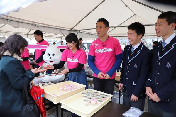 ピンクのTシャツを着たスタッフがデザートを販売し、その横で笑顔で写っている男子学生2名の写真