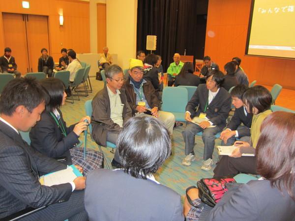 高校生と参加者がグループに分かれて円になって座っており、参加者の男性の話を回りに座っている高校生が真剣に聞いている様子の写真