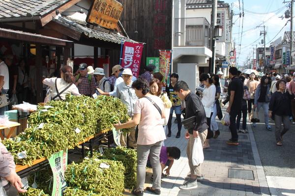 にぎやかな街の中店の外に並べれた沢山の黒枝豆と店を訪れた人々の写真