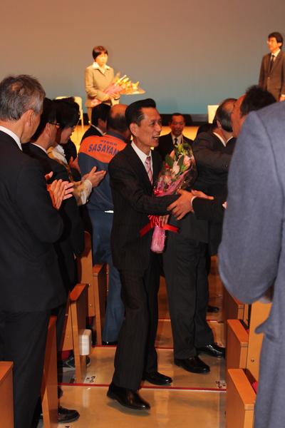 花束を持ち退場する退職者が、職員と順番に挨拶をしたり握手をしている写真