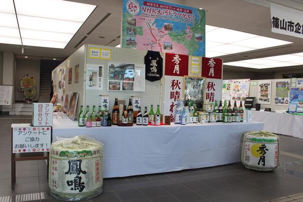 企業紹介展が開催されており、「NHK大河ドラマ化を」と書かれているパネルや、各企業のお酒や商品がの上に綺麗に並べられており、パネルで写真や絵を使って企業の取り組みを紹介している様子の写真