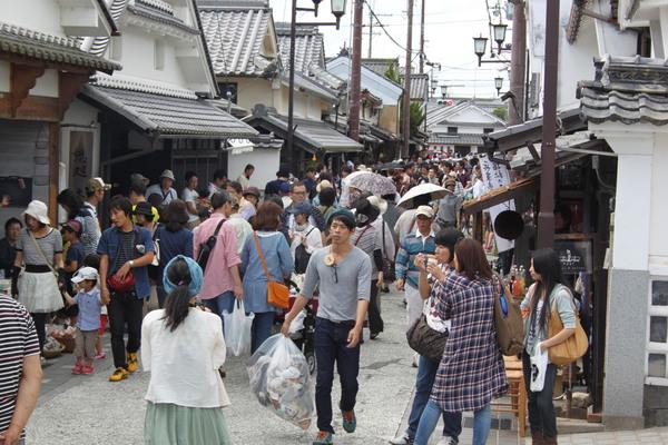 ササヤマルシェ会場で人ごみの中、緑のベレー帽を被った男性がごみ袋を片手に歩いている様子