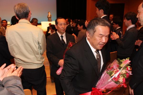 花束を持った退職者を、笑顔で見送る職員の写真