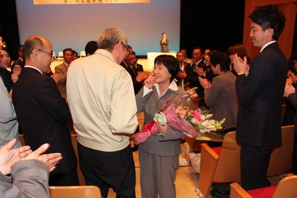 花束を持った女性退職者と、男性が笑顔で話をしている社員