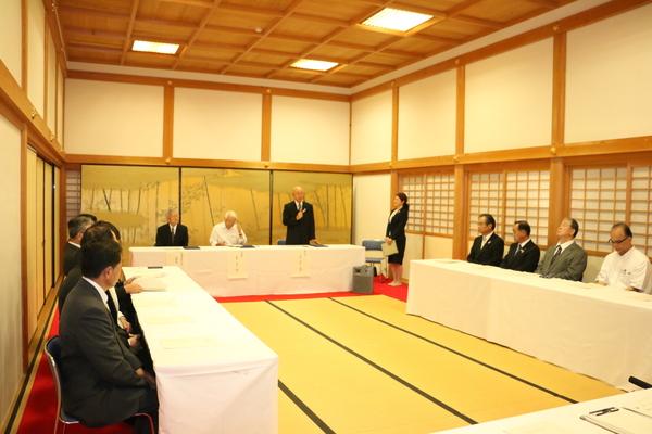 長机に白い布が敷かれその席に参加者が座り市長の話を聞いている写真