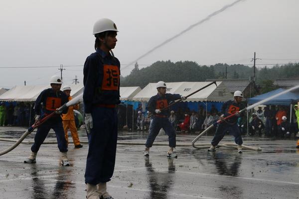 団員の方が1名立って周りでは2名の団員が放水している写真