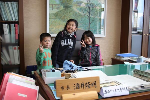 市長の席で、ピースサインをする笑顔の3人の子供の写真